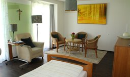 Eingerichtetes Zimmer mit Bett und einer Sitzgruppe. Großes gelbes Bild an der Wand. | © Susanne Wagner